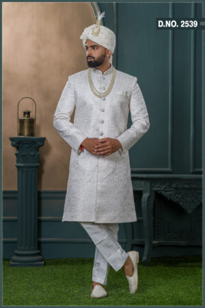 Ivory sherwani with intricate zari pattern, paired with an ivory turban featuring pearl and feather embellishment, and a layered pearl necklace.