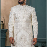 Ivory sherwani with intricate resham and sequin embroidery in floral and geometric patterns, paired with an ivory turban featuring pearl and feather embellishment.
