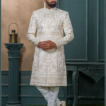 Ivory sherwani with intricate resham and sequin embroidery in floral and geometric patterns, paired with an ivory turban featuring pearl and feather embellishment.