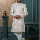 Ivory sherwani with intricate resham and sequin embroidery in floral and geometric patterns, paired with an ivory turban featuring pearl and feather embellishment.