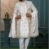 Ivory beige sherwani featuring geometric and floral embroidery with pink accents, paired with a white inner kurta and churidar.